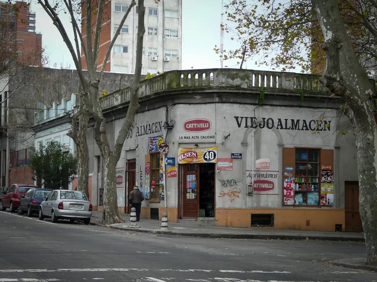 Almacén de barrio en una esquina de Montevideo con carteles de bebidas y productos en la vidriera