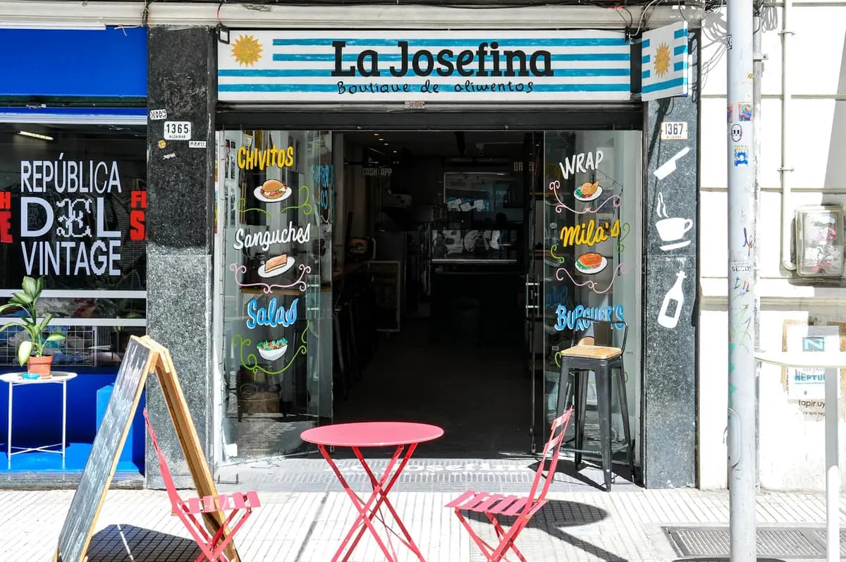 Frente de un café de Montevideo que ofrece chivitos y milanesas, con mesas rojas en la vereda