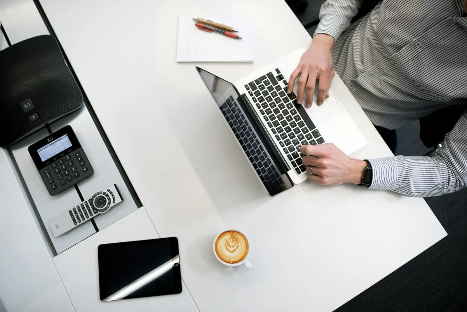 Vista cenital de una persona trabajando con una portátil, un posnet y un café sobre una mesa blanca