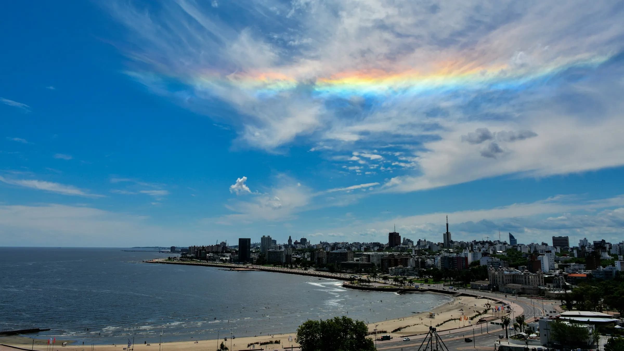 Vista aérea de la rambla de Montevideo con la playa, la ciudad y un cielo con nubes iridiscentes